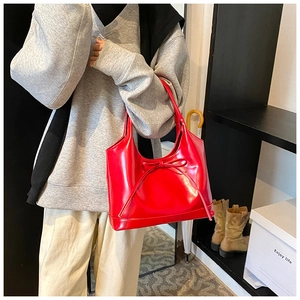 Detail of red patent leather tote bag with bow decoration worn by a fashion model