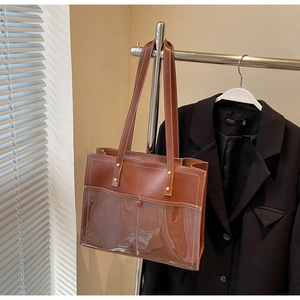 Detail of a brown leather and PVC tote bag with metallic studs hanging on a metal stand