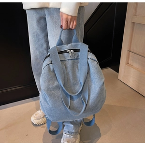 Close-up of light blue washed denim backpack with silver dual zippers and sturdy handle