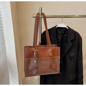 Detail of retro brown leather tote with transparent PVC pocket and woven bell charm