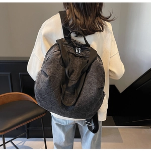 Detail of the large denim backpack with wide straps and top handles on a model
