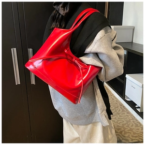 Model wearing a glossy red shoulder bag with a bow detail and patent leather finish