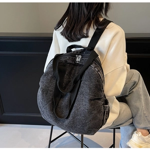 Detail of a large black washed denim backpack shown on model against a minimal wall