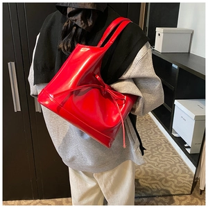 Model wearing a red patent leather tote bag with a bow detail in a home setting