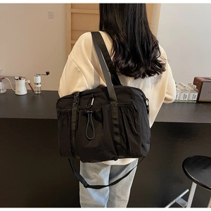 Close-up of black nylon tote bag with wide strap and drawstring detail on model