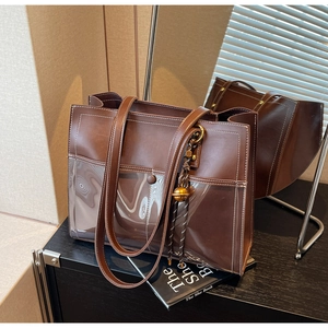 Detailed view of brown PU leather tote with contrast stitching and golden ball pendant