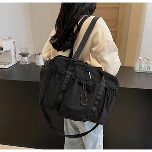 Detailed side view of a large black nylon tote bag with functional pockets and wide straps