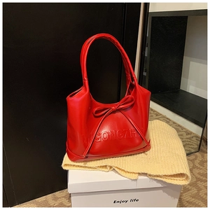 Close-up of red glossy handbag featuring a large bow and embossed letter details
