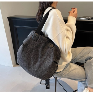 Detail of grey plush tote bag featuring wide black shoulder strap and leather patch accents