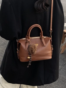 Brown PU leather boston pillow bag with pompom charm shown on a model in black coat