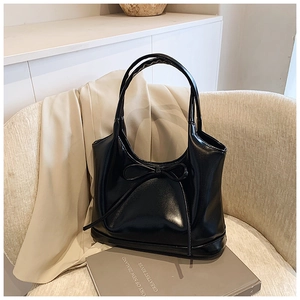 Close-up of black glossy leather tote bag with a bow detail on a beige chair