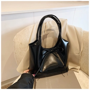 Detailed shot of glossy black faux leather handbag with elegant slim bow decoration