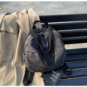 Close-up of retro washed black denim backpack with side pocket on a black wooden bench