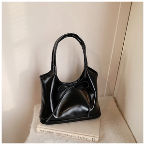 Close-up of black patent leather tote bag with stylish bow ribbon on a soft white fabric