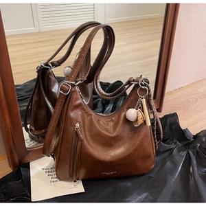 Detail of soft brown leather tote with adjustable strap and vintage baseball charm
