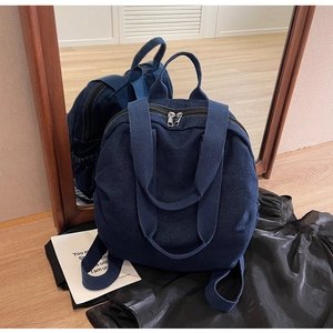 Detail view of large dark blue denim backpack with dual handles and metal zipper closure