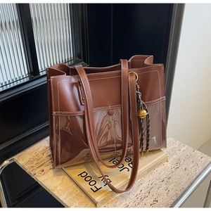 Detail of a brown leather and transparent PVC tote bag with white stitching and a bell charm