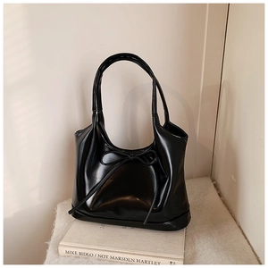 Detail of a black glossy leather shoulder bag with a delicate bow on a white book