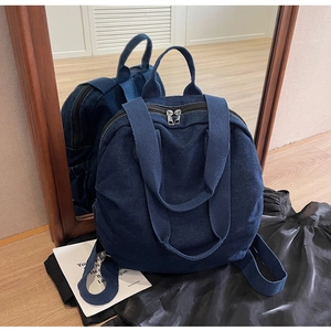 Deep blue denim backpack with dual zipper and top handle shown in a mirror reflection