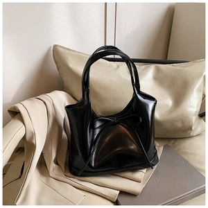Detail of a black patent leather shoulder bag featuring a stylish bow and glossy finish