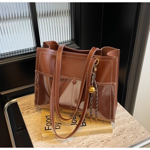 Detail of a brown leather and transparent PVC tote bag with white stitching and gold charm