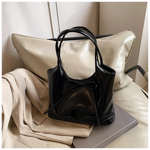 Detail of black glossy leather handbag featuring a delicate ribbon bow decoration