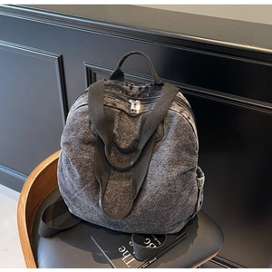 Detail of vintage grey acid wash denim backpack with silver zipper on a wooden chair