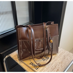Detail of brown leather and PVC tote bag with white stitching and gold ball charm