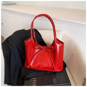 Detail of red shoulder bag with bow decor and embossed lettering on high-quality leather