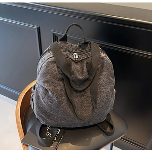 Detail of dark grey washed denim backpack with double zippers on a black leather chair