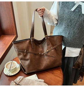 Detail of a large brown faux leather tote bag with gold hardware and shoulder straps