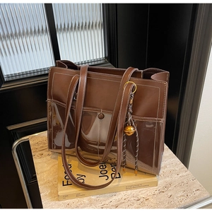 Detail of a brown leather tote bag featuring white stitching and a gold bell charm