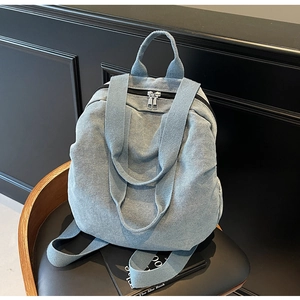 Close-up of light blue denim backpack with durable silver metal zippers and top handle