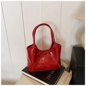 Detailed view of red tote bag featuring bow accent and embossed lettering on leather
