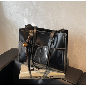 Detail of black leather and PVC tote bag with white stitching and woven bell charm