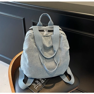 Detail of light blue denim backpack with silver dual zippers on a vintage chair