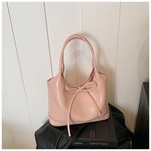 Detailed view of pink leather tote bag featuring a decorative bow on textured surface