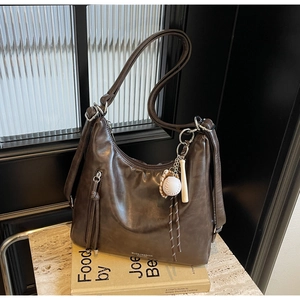 Close-up of brown hobo tote bag with baseball tassel charm on vintage books