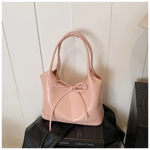 Detail of pink leather tote bag with bow detail on a black garment with a book