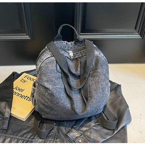Detailed close-up of dark grey washed denim backpack with wide straps and silver zippers