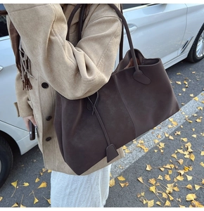 Detail of dark brown faux suede tote bag with slim shoulder strap and leather tag