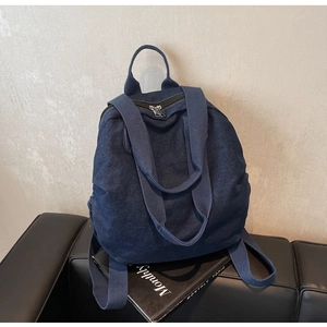 Close-up of deep blue denim backpack with silver metal zipper on stylish magazine backdrop