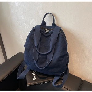 Detail of the blue denim backpack featuring dual metal zippers and a top carry handle