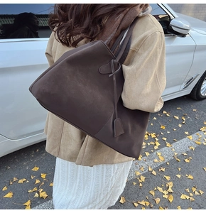 Detail of dark brown suede tote bag with decorative square charm in autumn setting