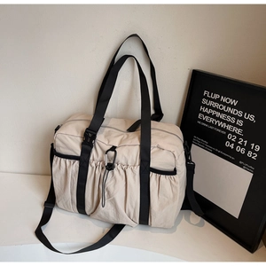 Detail of beige nylon tote bag with black wide straps, utility carabiner and drawstring pocket