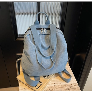 Detail of light blue denim backpack showing dual metal zippers and canvas strap design