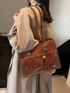 Brown tote bag with white stitching and bell charm shown on a shoulder in a modern room