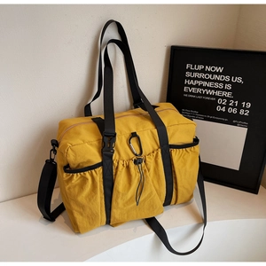 Detail of a mustard yellow nylon tote bag featuring elastic drawstring side pockets and carabiner