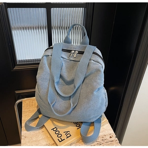Close-up of light blue denim backpack with double zippers on a textured stone surface