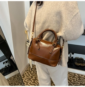 Close-up of a glossy dark brown Boston bag featuring golden hardware and leather texture